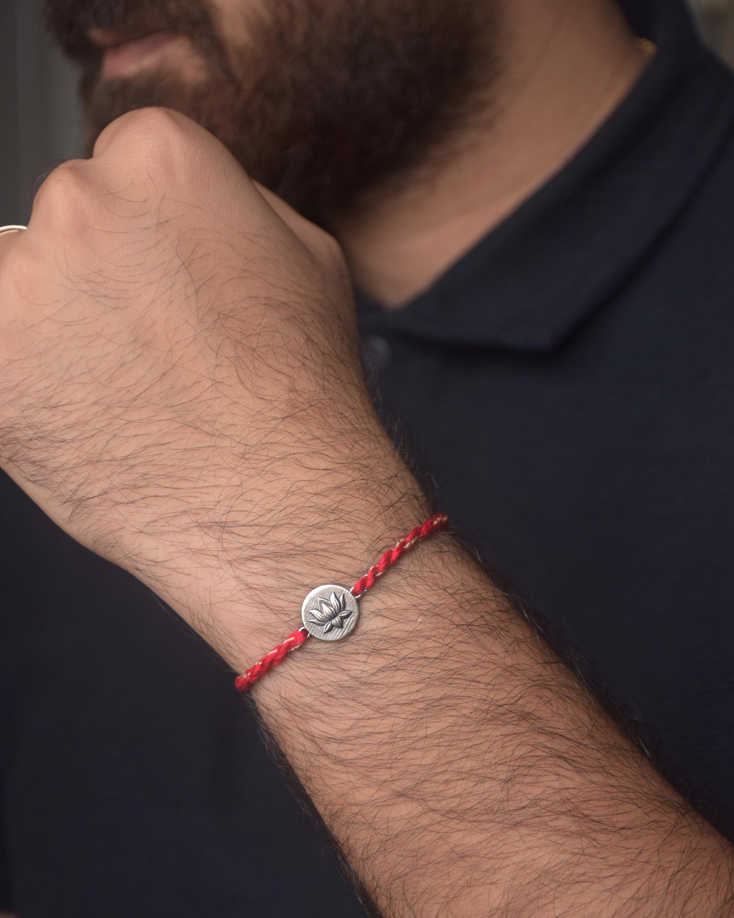 Red cotton thread rakhi with a silver charm on a person's wrist against a dark background