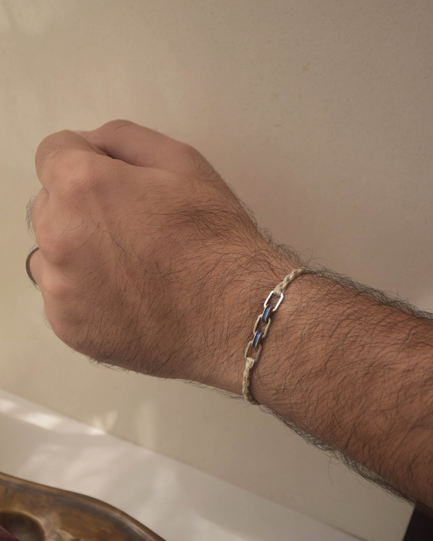 Hand wearing a silver Rakhi on a neutral background