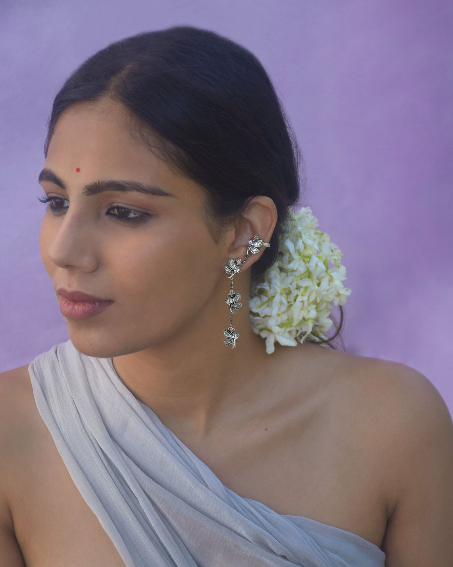Madhura Earrings crafted in 92.5 sterling silver featuring four flower-inspired motifs adorned with radiant jadau stones connected by delicate silver chains for a cascading effect. One motif includes a secure clip to wear as an ear cuff.