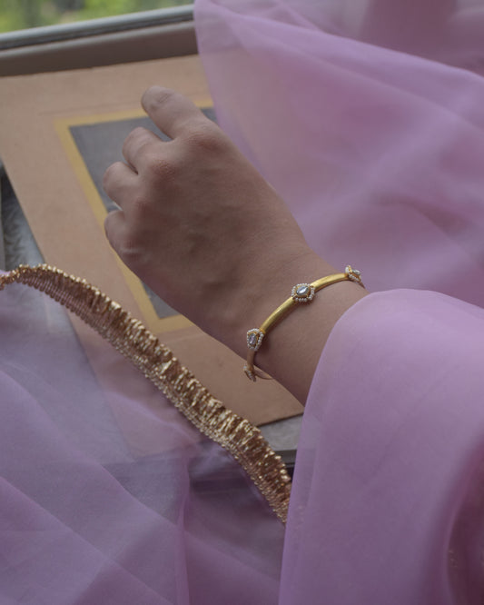 Sukanya Bangle crafted in 925 silver with gold polish, featuring seven white Jadau stones surrounded by delicate seed pearls.