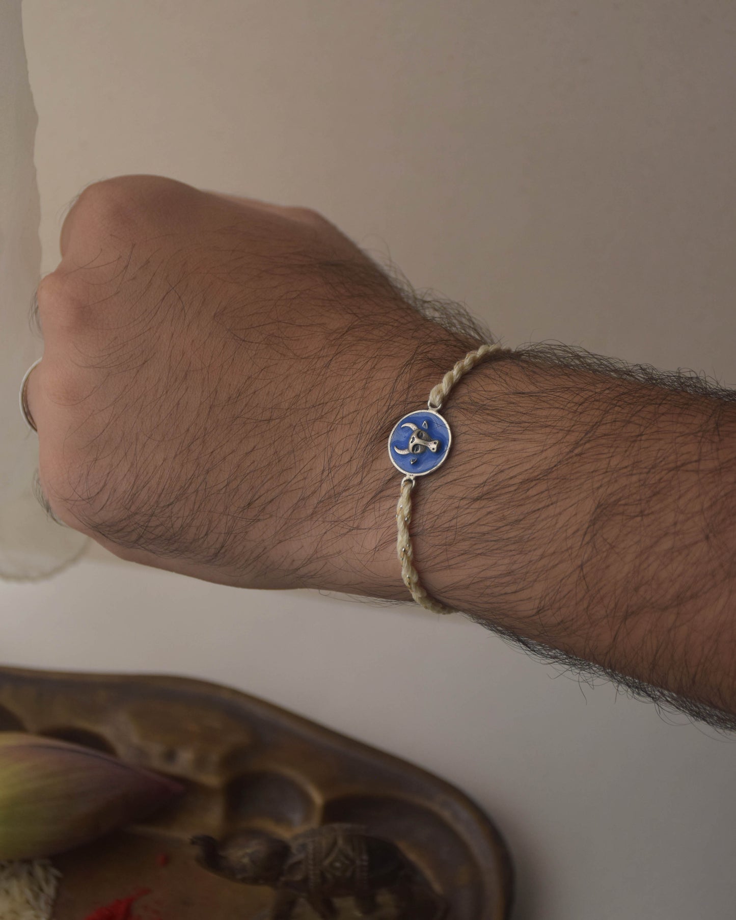 Hand wearing 925 Silver Rakhi with blue Nandi motif on a card with 'NUVI' branding, placed on a textured surface.
