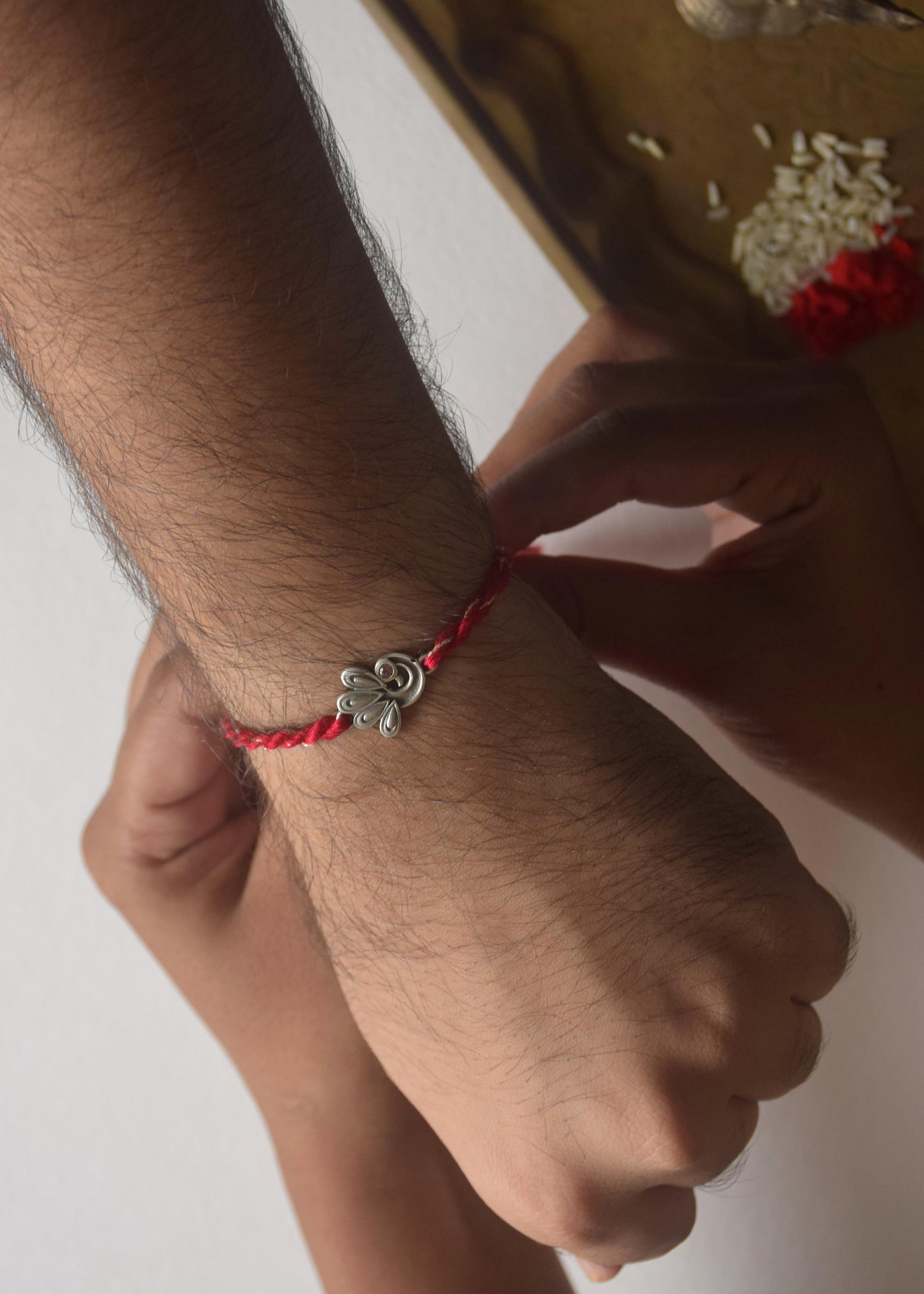 Hand wearing a peacock motif Silver Rakhi with a red cotton thread on a white background.