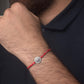 Red cotton thread rakhi with a silver charm on a person's wrist against a dark background
