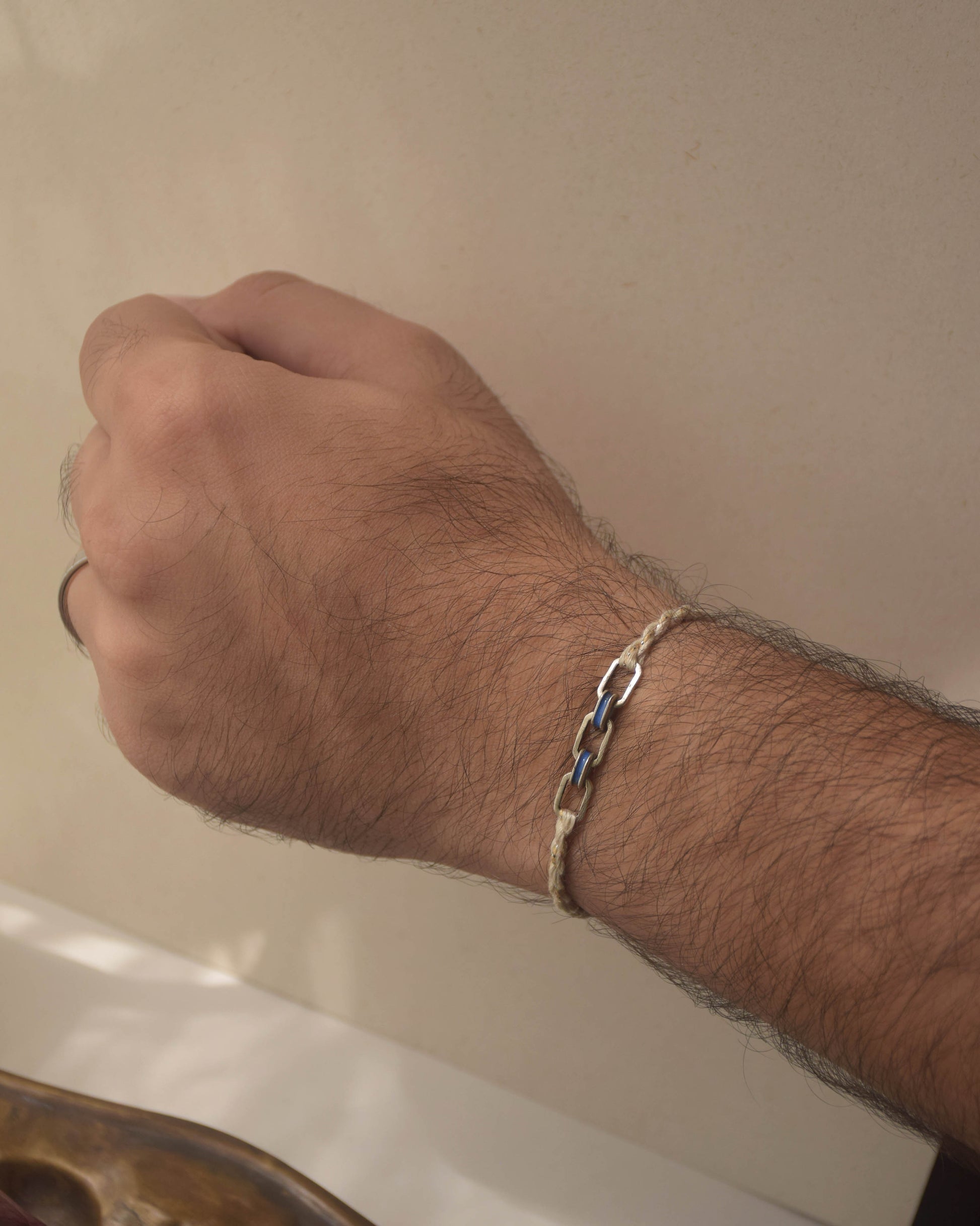Hand wearing a silver Rakhi on a neutral background