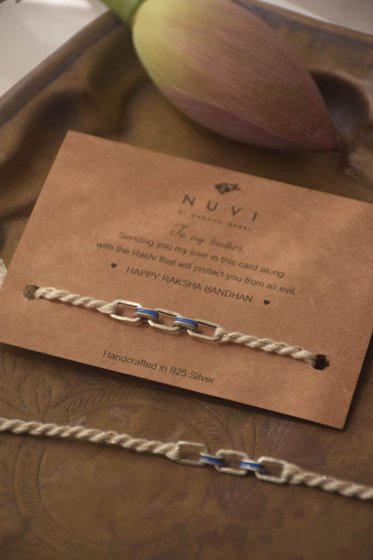 Sterling silver rakhi with blue enamel detailing on a brown card with 'NUVI' branding and text