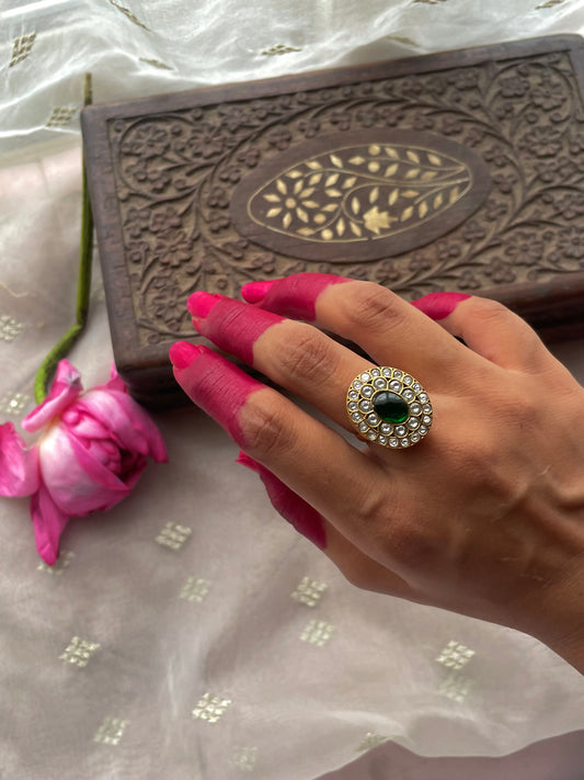 Damini Ring featuring a vibrant green center stone surrounded by a halo of sparkling white stones arranged in an elegant floral pattern.