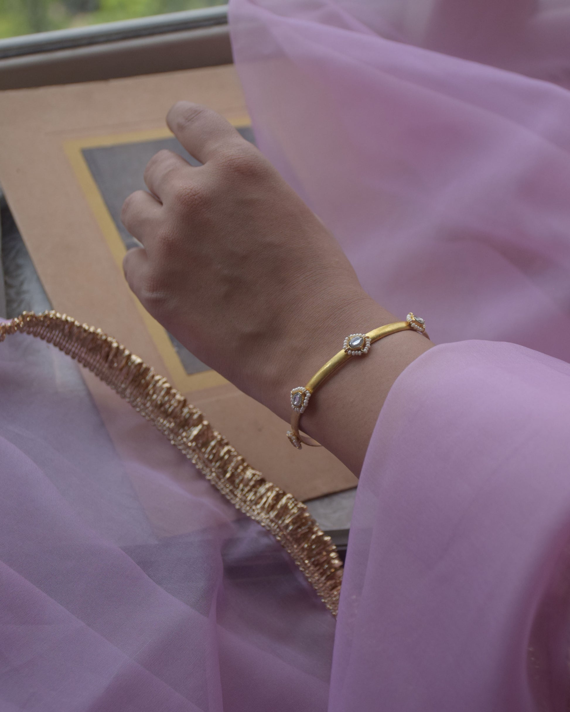 Sukanya Bangle crafted in 925 silver with gold polish, featuring seven white Jadau stones surrounded by delicate seed pearls.