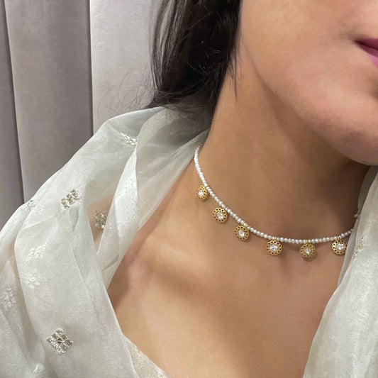 BindiyA Necklace crafted in 925 silver with lustrous gold polish, featuring nine intricately designed units each adorned with a white jadau stone and gold wire work, suspended on a string of delicate freshwater pearls 