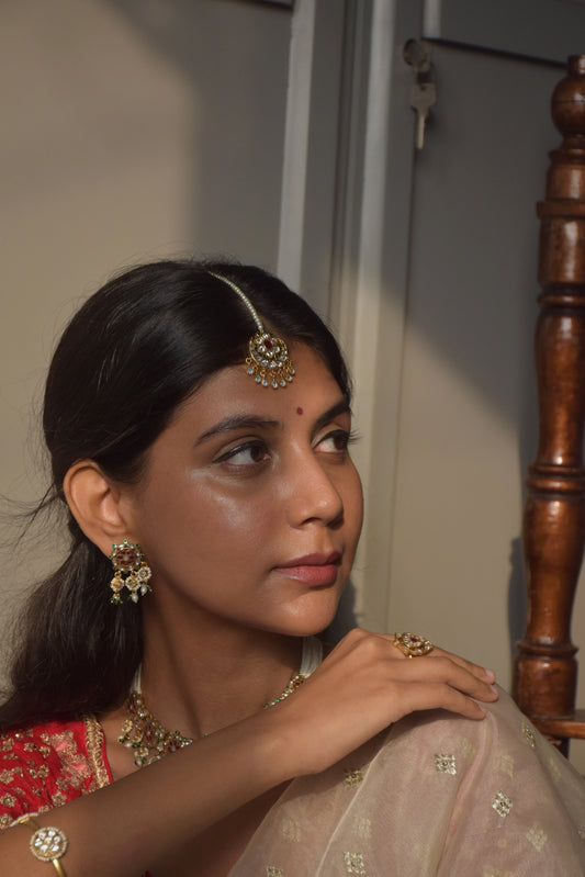 Chandphool Maangtika in traditional design featuring a crescent-shaped Chand motif adorned with Jadau stones, strung on a line of pearls with antique-style trinket drops.