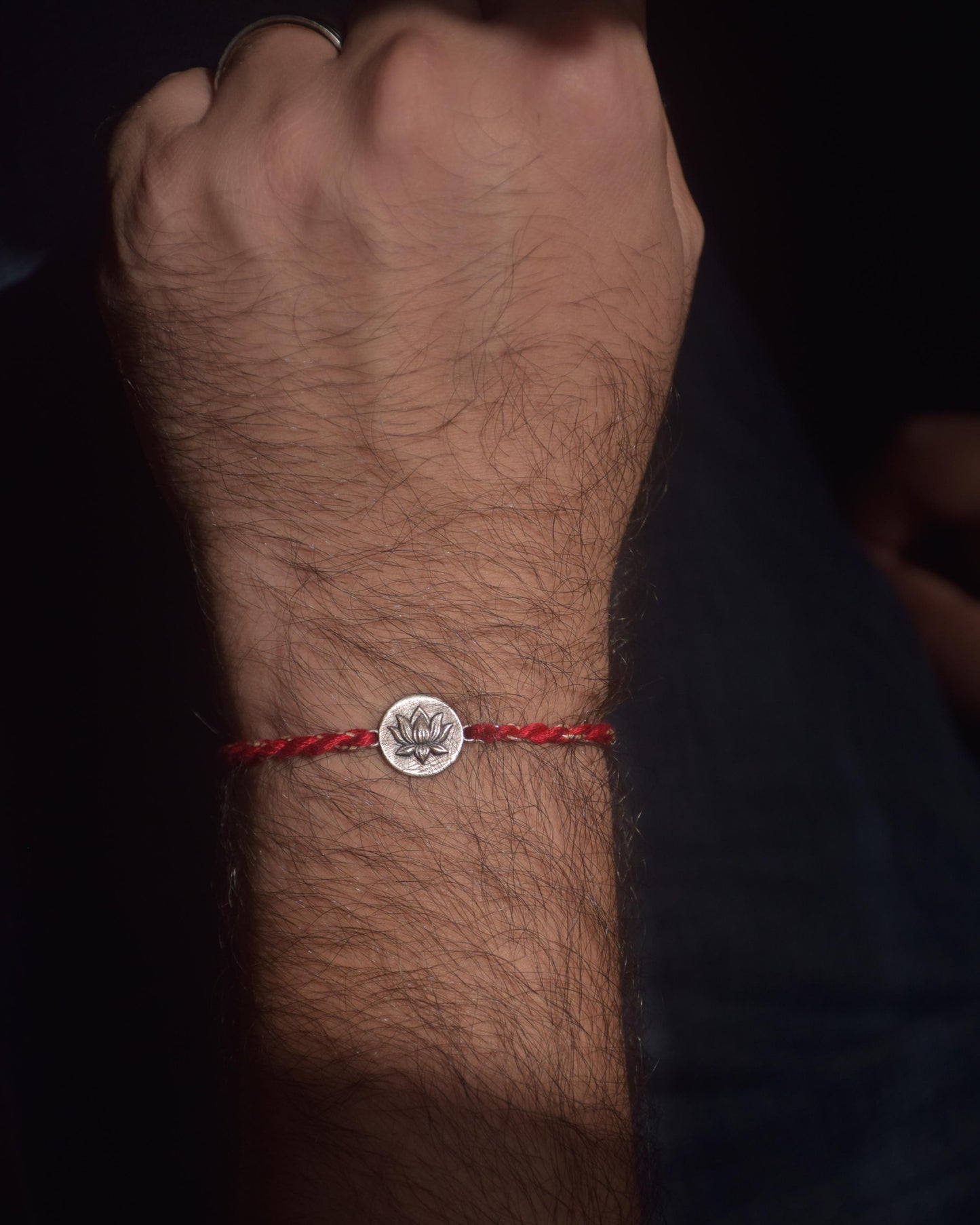 Red string bracelet with a lotus silver charm on a wrist