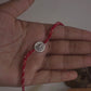 Hand wearing a red cotton thread Rakhi with a silver lotus flower charm.
