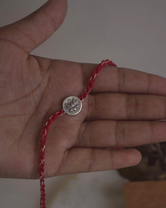 Hand wearing a red cotton thread Rakhi with a silver lotus flower charm.