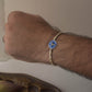 Hand wearing 925 Silver Rakhi with blue Nandi motif on a card with 'NUVI' branding, placed on a textured surface.