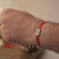 Hand wearing a Silver Om Rakhi with red cotton thread on a neutral background
