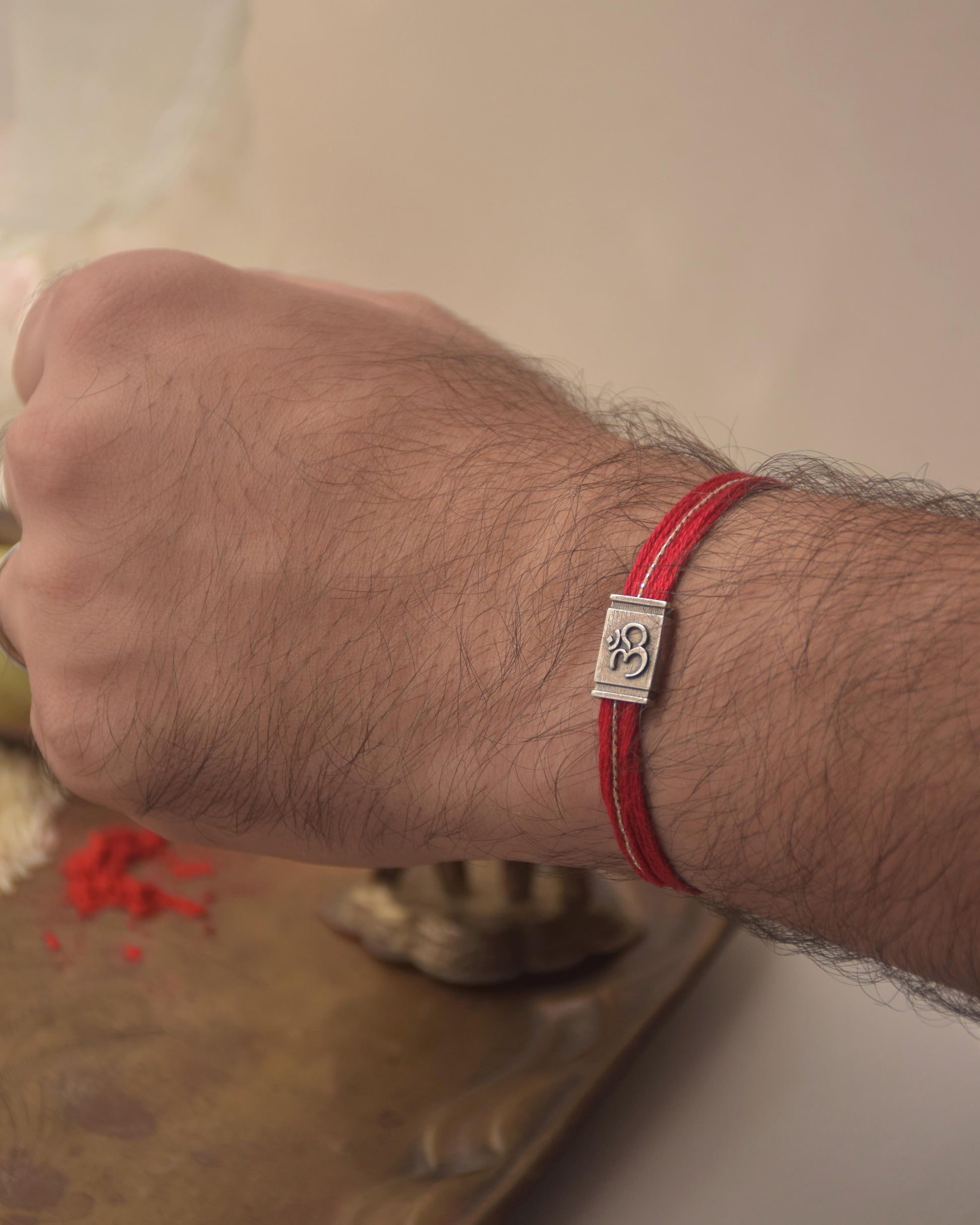 Hand wearing a Silver Om Rakhi with red cotton thread on a neutral background