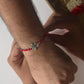Hand wearing a peacock motif Silver Rakhi with a red cotton thread on a white background.