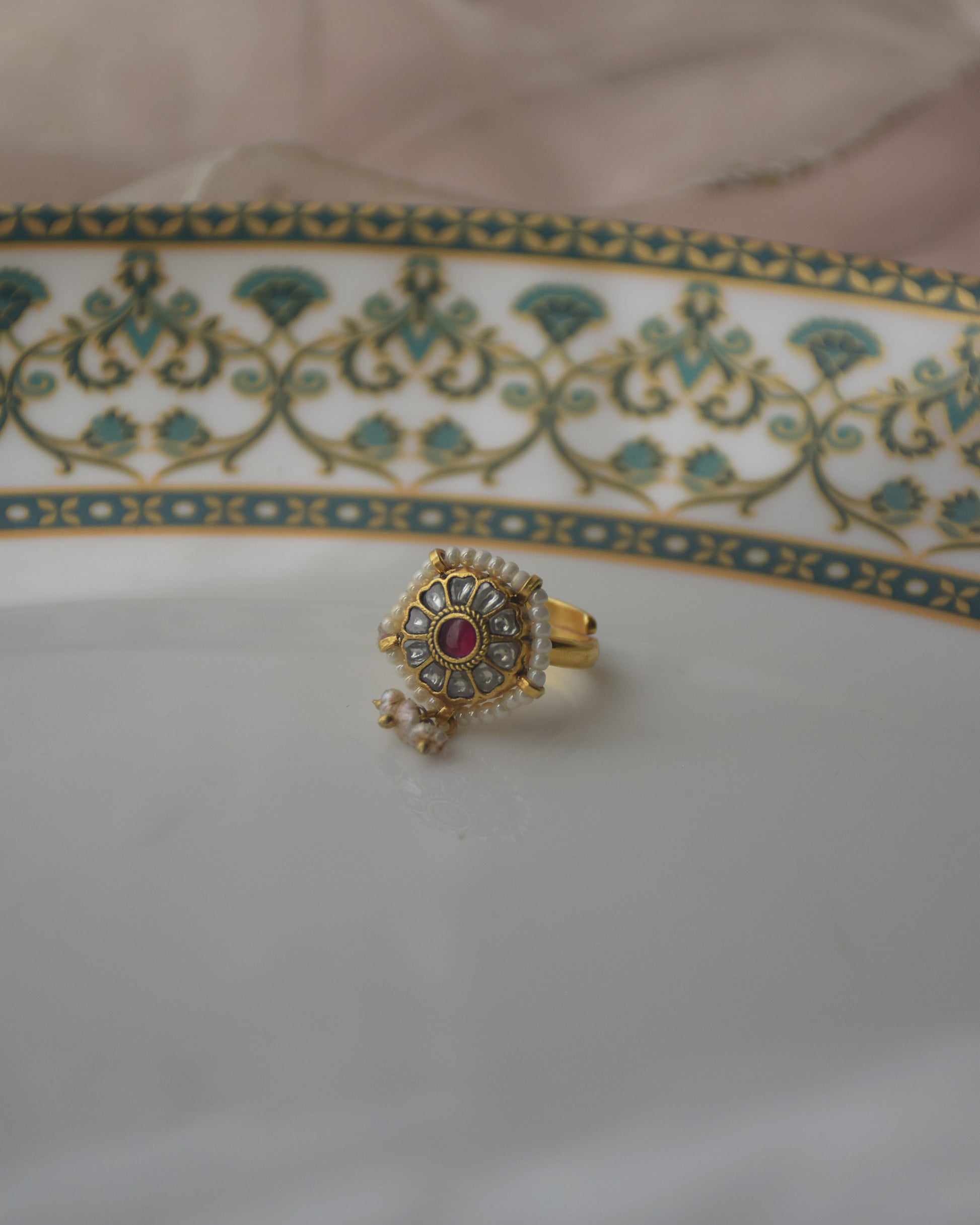 Sarayu Ring - Crafted in 92.5 gold plated silver with white jadau stones studded on a flower motif with red stone in centre & a line of seed pearl around it.