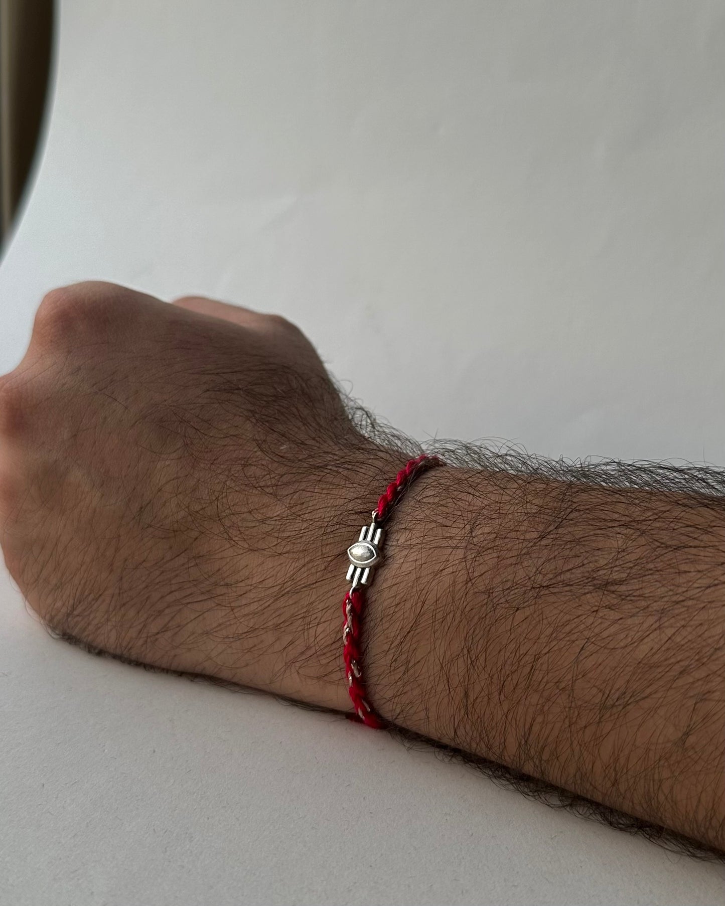 Red cootn thread Rakhi with 925 Silver unit on a wrist with a neutral background