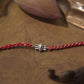 Red braided cotton thread with a silver motif inspired from Shivji's Thire Eye.