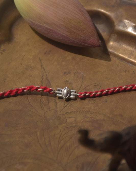 Red braided cotton thread with a silver motif inspired from Shivji's Thire Eye.