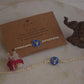 925 Silver Rakhi with blue enamel and Nandi motif on a card with 'NUVI' branding, placed on a textured surface.