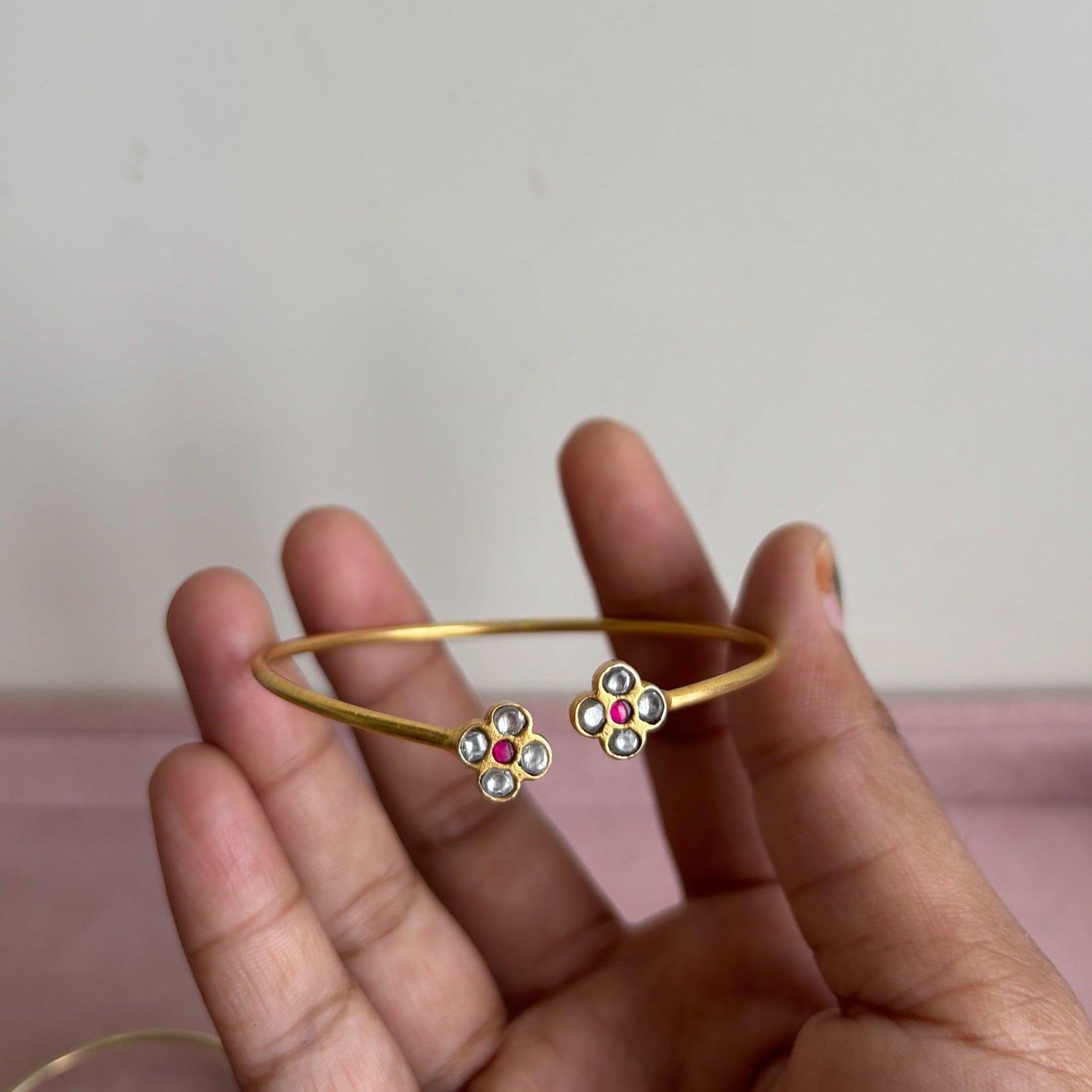 Gold bangles with floral designs held in a hand against a neutral background