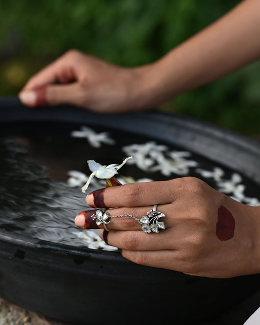 Tarini dual finger ring in 92.5 sterling silver featuring adjustable rings connected by a delicate chain, adorned with floral motifs and jadau stones.